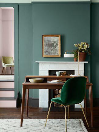 Office space featuring light pink chairs, muted green (Pleat) walls, marble fireplace, wooden desk and green velvet chair.