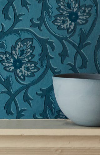 Deep blue foliage pattern Hoja - Air Force Blue wallpaper behind a shelf with a bowl and a pile of old books.