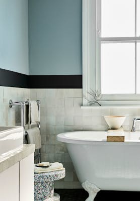 Bathroom with pale blue (Bone China Blue) upper walls and white tiles underneath, next to bathtub, window and sink.