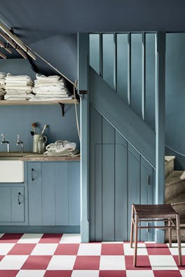 Laundry room painted in muted blue 'Etruria' with a sink, staircase and checkered floor tiles.