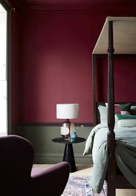 Deep red (Baked Cherry) bedroom with a contrasting dark green lower wall behind a four poster bed and armchair.