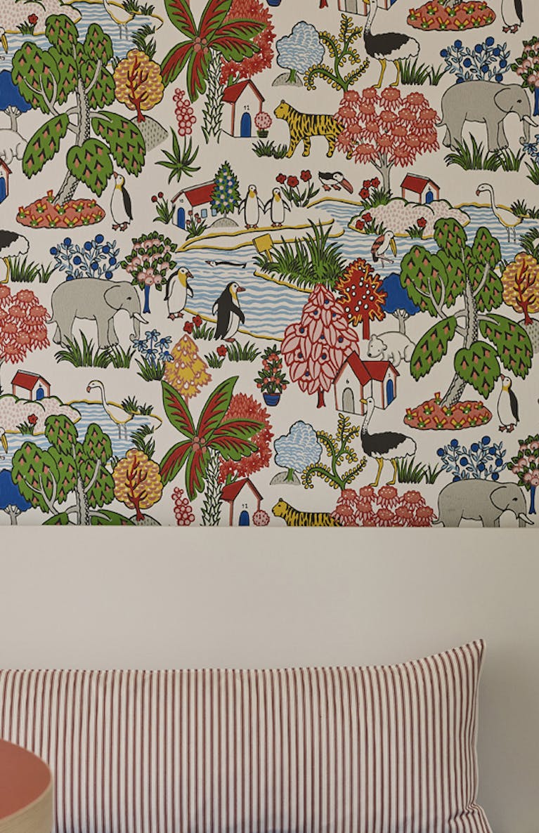 Breakfast room featuring multi-coloured wildlife print wallpaper (Animal Kingdom - Atomic Red) with a bright red table and wicker chairs next to a banquette.