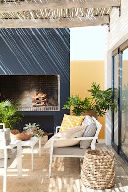 Outside seating area with blue-black (Basalt) and mustard yellow (Bassoon) walls, cushions, plants and a wicker basket.