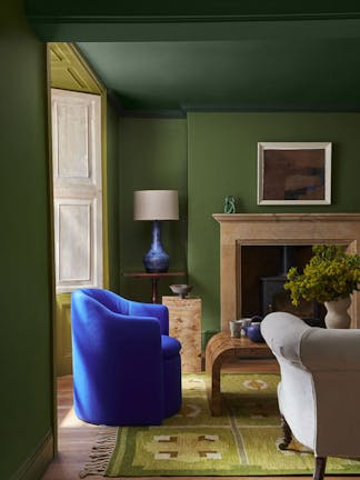 Living room painted in deep green 'Hopper' with a dark green ceiling above a fireplace and a bright blue armchair.