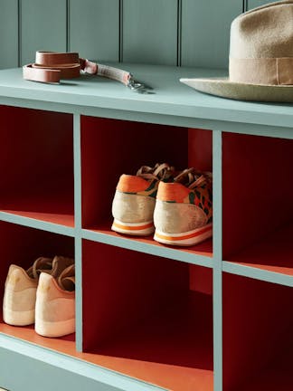 A panelled wood wall and shoe rack painted in green (Pleat), with contrasting deep red (Heat) shelving.