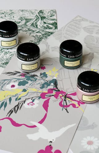 Four Little Greene sample paint pots in French Grey, Wood Ash, Three Farm Green and Hellebore on top of wallpaper samples.