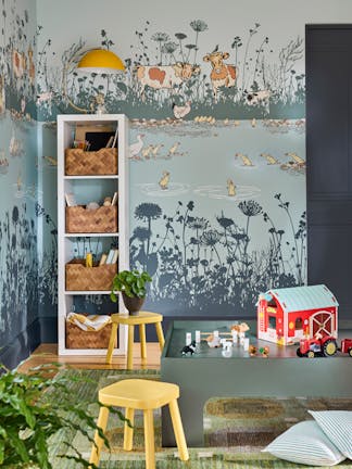 Children's playroom featuring blue mural wallpaper (Riverside Capers - Moo) with storage space to the left alongside yellow stools and toys in the foreground.