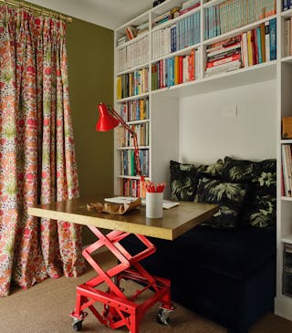 Colorful study with green left wall with a bright floral curtain and a white right wall with a bookcase.