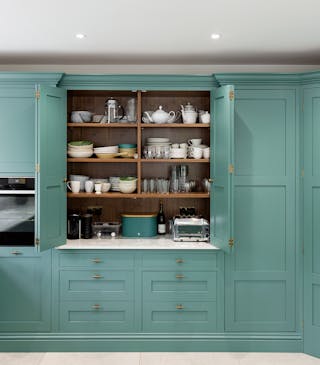 Luxury green (Pleat) kitchen cupboards with the middle ones open, revealing shelves containing bowls and plates.