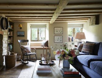 Living room with a low ceiling with beams, brick wall to the left and a blue sofa to the right topped with checked cushions.