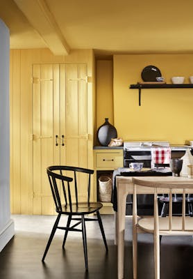 Kitchen color drenched in vibrant yellow shade 'Giallo', with a wooden table and chairs.