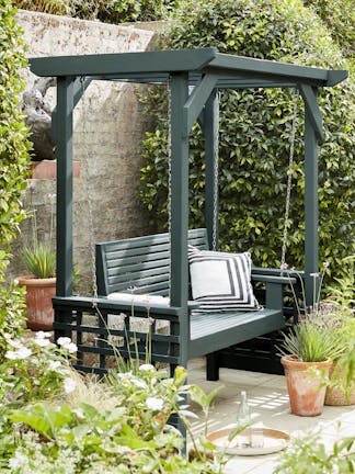 Deep green blue (Harley Green) garden swing seat surrounded by foliage and terracotta plant pots.