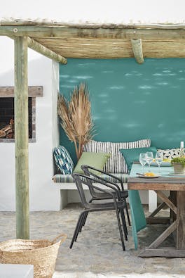 Outdoor table and chairs under a bamboo roof with the back wall painted in blue-green shade 'Canton'.