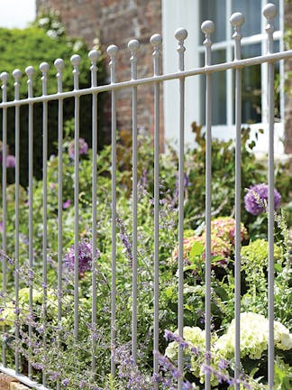 Metal railings outside of a house painted in mid gray shade 'Lead Color' with flowers and plants behind.