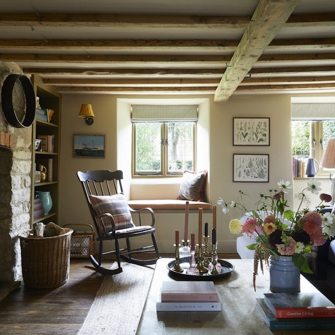 Living room with a low ceiling with beams, brick wall to the left and a blue sofa to the right topped with checked cushions.