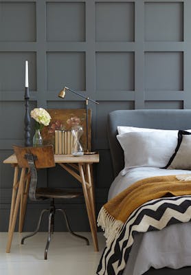 Paneled bedroom painted in dark grey 'Scree' with a small wooden desk next to a grey bed on a white floor.