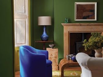 Living room painted in deep green 'Hopper' with a dark green ceiling above a fireplace and a bright blue armchair.