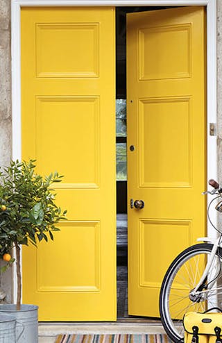 Front door painted in bright yellow 'Mister David' with two trees and a bike under pillars.