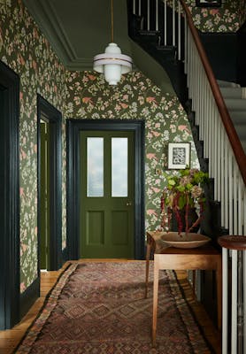 High ceiling hallway featuring dark green floral wallpaper (Aderyn - Olive Colour) with dark green woodwork and a tapestry rug.