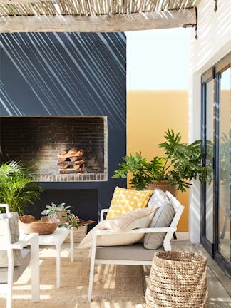 Outside seating area with blue-black (Basalt) and mustard yellow (Bassoon) walls, cushions, plants and a wicker basket.