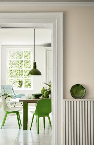 Hallway looking into a dining room painted in beige shade Portland Stone - Dark with bright green dining room chairs.