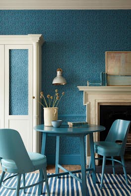 Dining space with a tonal blue wallpaper (Hoja - Air Force Blue) and white (Shirting) cupboard with blue table and chairs.