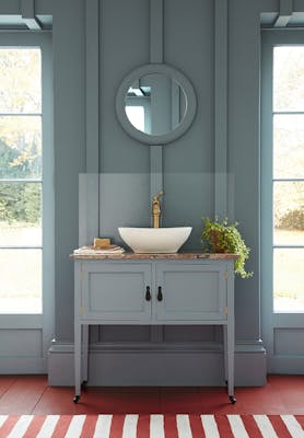 Cloakroom painted in muted blue shade 'Etruria' with a basin and round mirror in the center of two large windows.