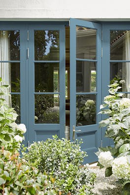 Back door painted in rich blue 'Air Force Blue' looking into a house, with plants and trees surrounding.