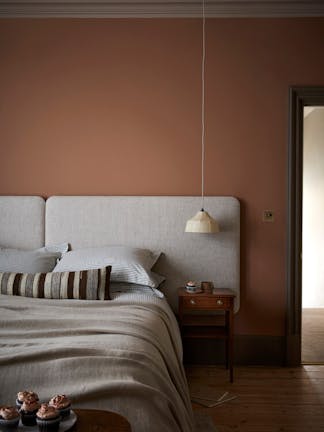 Bedroom painted in muted pink shade 'Split Pink' with a double bed next to a wooden sidetable.