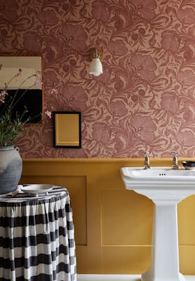 Bathroom with two-tone wall decor, featuring Poppy Trail pink floral wallpaper above and a mustard colour paint below.