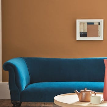 Living space painted in dark orange (Middle Buff) with a contrasting deep blue sofa and wooden table on a rug.