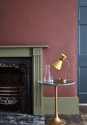 Living room wall painted in plum purple shade 'Adventurer' with a sage green fireplace and a wooden floor.