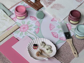 Pink and light green themed mood board featuring a floral patterned wallpaper sample, various fabric samples and color cards.