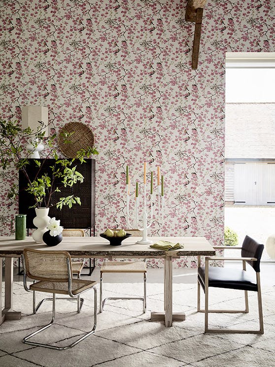 Dining room with pink printed floral and bird wallpaper (Massingberd Blossom - Mineral) and wooden dining table and chairs.