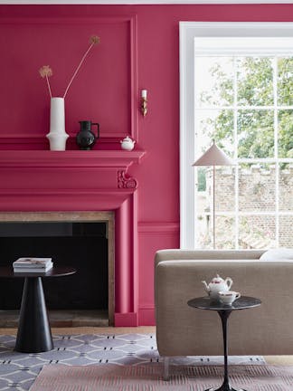 Living space painted in bright pink 'Leather' with a matching fireplace and  constrasting white window frame and an armchair.