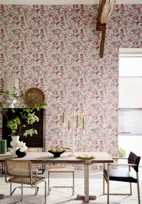 Dining room with pink printed floral and bird wallpaper (Massingberd Blossom - Mineral) and wooden dining table and chairs.