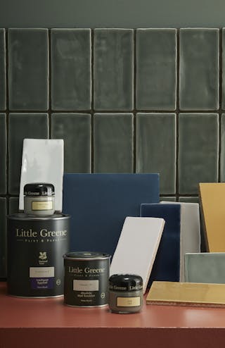 Little Greene paint tins, sample pots and individual tiles placed on a bright orange surface.