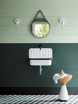 Paneled bathroom with the upper wall painted in Aquamarine and lower wall in dark green with a white sink and round mirror.