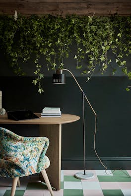 Home office with a dark green wall (Obsidian Green) with plants hanging from the ceiling alongside a wooden table and chair.