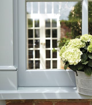 Close-up of the bottom of a front door painted in a grey-blue color and a bucket of white flowers on the right-hand side.