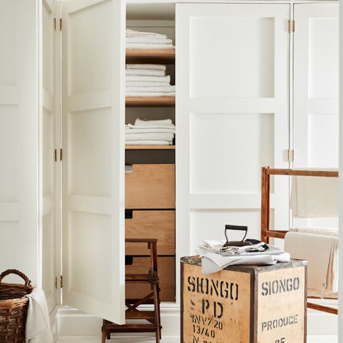 Laundry room color drenched in off white 'Linen Wash' with the closet door opened showing wooden drawers and folded laundry.