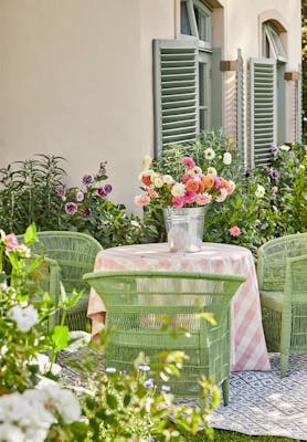 Outside dining area with three bright green garden chairs and a warm neutral wall (Clay) surrounded by flowers and greenery.