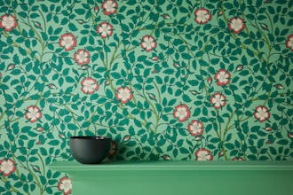 Close-up of green floral wallpaper (Briar Rose - Green Verditer) with a fireplace surround painted in a deep green shade. 