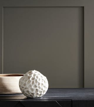 Close-up of wall paneling in a neutral brown shade (Rolling Fog) behind a wooden bowl and stone-colored ornament.