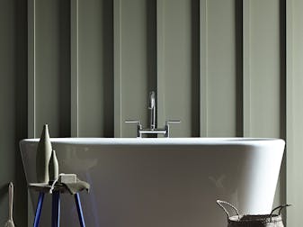 Close up of a panelled bathroom, painted in deep grey-green, with a large freestanding white bathtub.