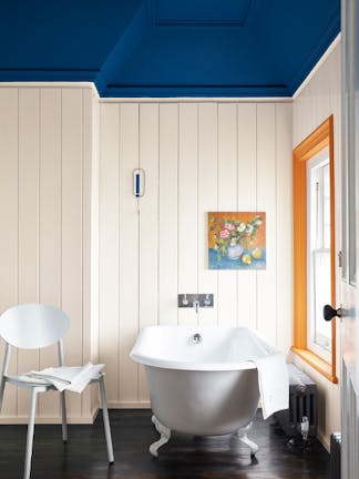 Bathroom with paneled off-white (Flint) walls and a contrasting deep blue ceiling with a bathtub and chair by the window.