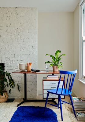 Home office with pale taupe brickwork wall (Joanna), a vibrant blue wooden chair and a matching rug in front of wooden desk.