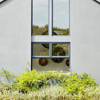 House exterior with large windows painted in mid grey (Urbane Grey) with bright yellow garden chair and plants.