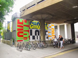 Brightly colored mural featuring the words 'Choose Love' painted on a wall with bikes parked in front and women walking past.