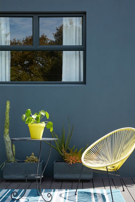 Outside dining area with a dark blue wall (Hicks' Blue) and bright yellow chair with a small table and plants.
